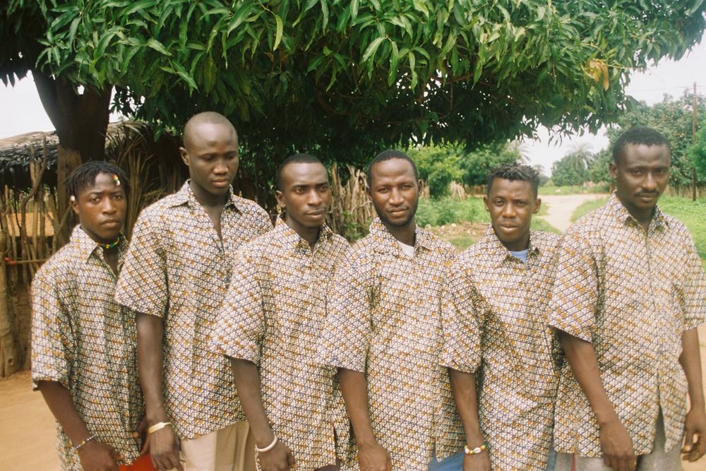 Six men in matching patterned shirts standing in a row