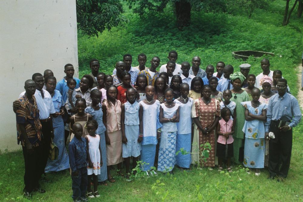 A large choir standing on grass in front of a white wall