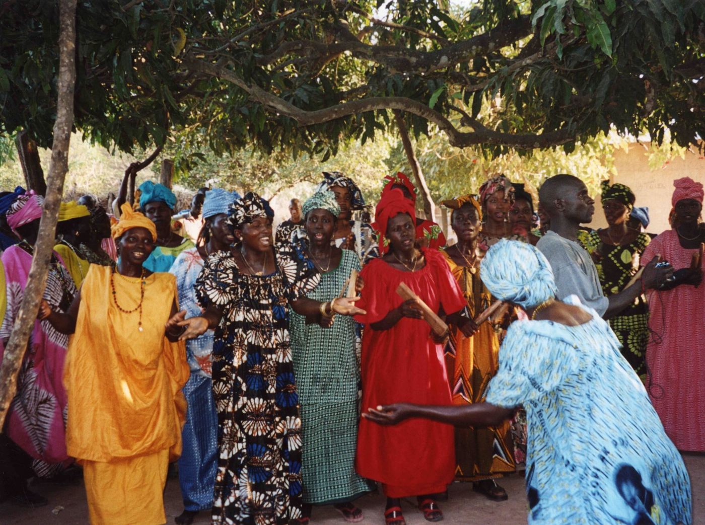 Women in bright cloth singing and dancing under a tree